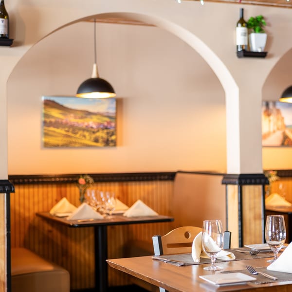 Restaurant interior with set tables, arched doorways, and wall art depicting landscapes.