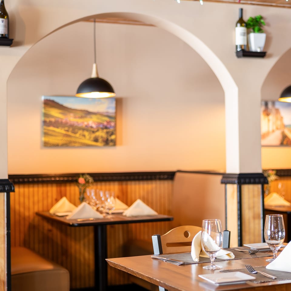 Restaurant interior with set tables, arched doorways, and wall art depicting landscapes.