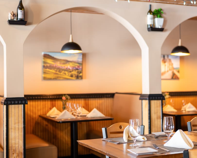 Restaurant interior with set tables, arched doorways, and wall art depicting landscapes.