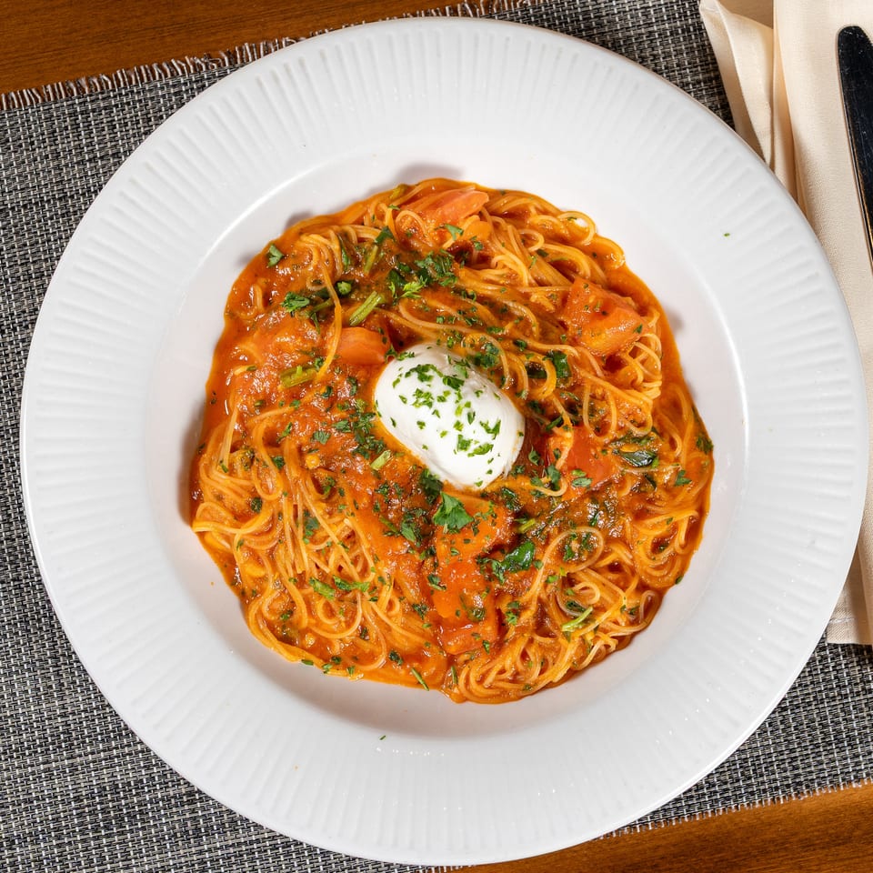 Spaghetti with tomato sauce, shrimp, and a dollop of white cream cheese, garnished with parsley.