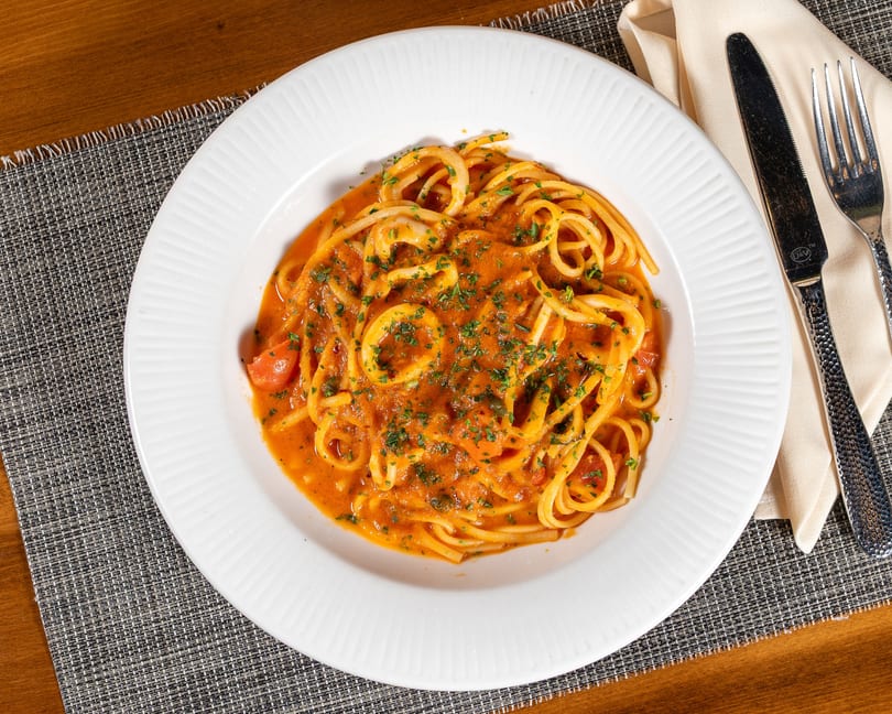 Spaghetti with calamari and tomato sauce, garnished with parsley, on a white plate with cutlery.