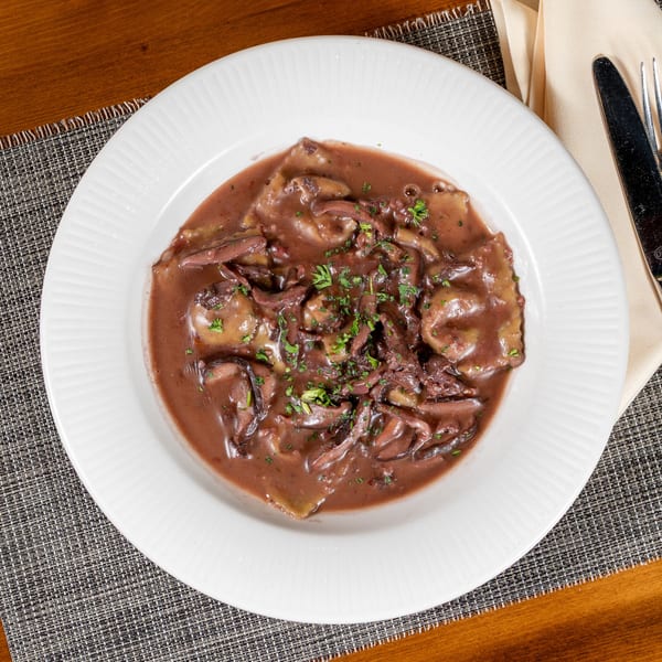 Ravioli in a rich red wine sauce with mushrooms and fresh parsley on a white plate.