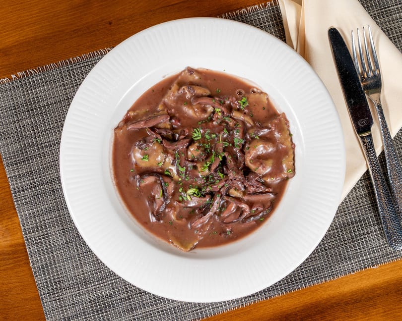 Ravioli in a rich red wine sauce with mushrooms and fresh parsley on a white plate.
