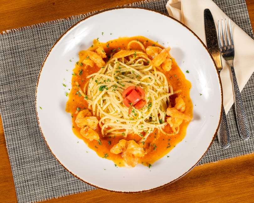 Spaghetti with shrimp in a red sauce, garnished with parsley and a tomato flower.