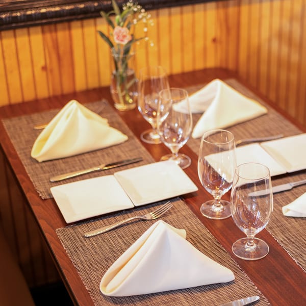 A set table with white napkins, plates, silverware, and wine glasses, with a small vase of flowers.