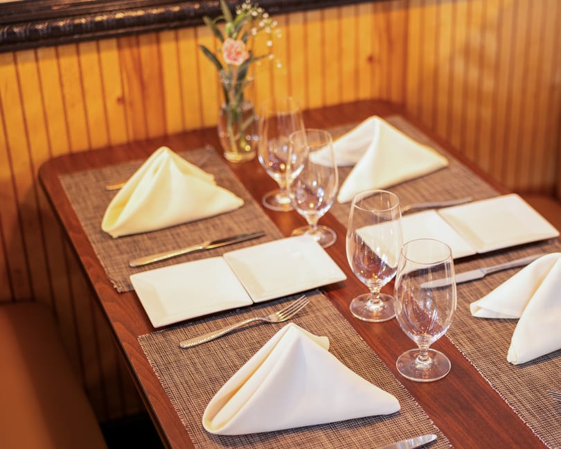 A set table with white napkins, plates, silverware, and wine glasses, with a small vase of flowers.