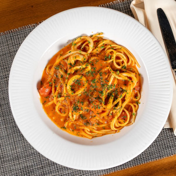 Spaghetti with calamari and tomato sauce, garnished with parsley, on a white plate with cutlery.