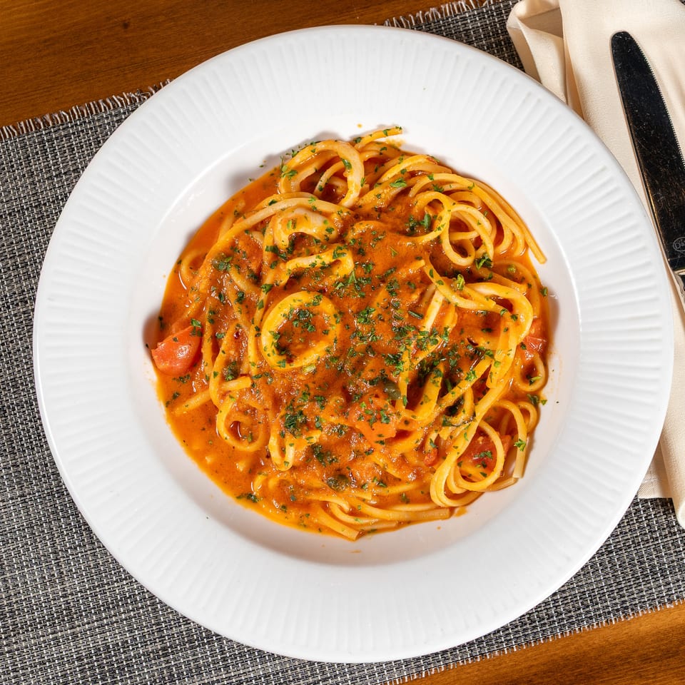 Spaghetti with calamari and tomato sauce, garnished with parsley, on a white plate with cutlery.