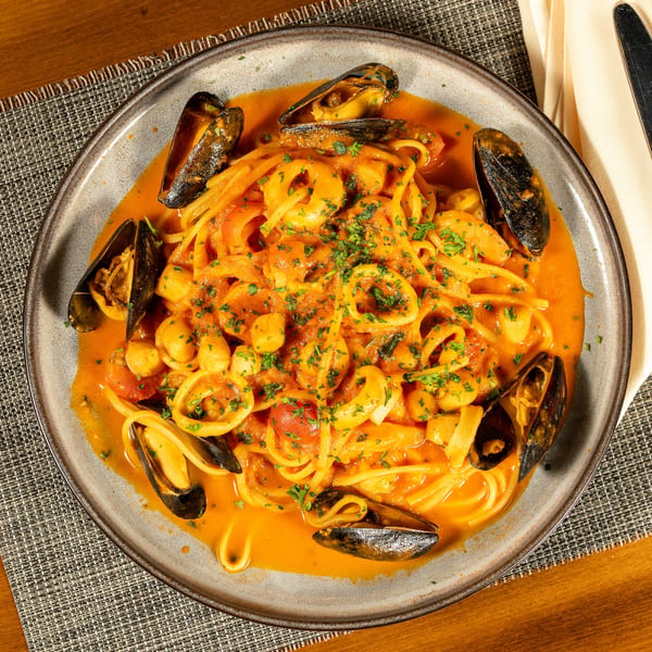 Seafood pasta with mussels, calamari, and scallops in a rich tomato sauce, garnished with parsley.