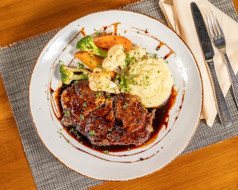 Two cuts of steak with gravy, mashed potatoes, broccoli, carrots, and cauliflower on a white plate.