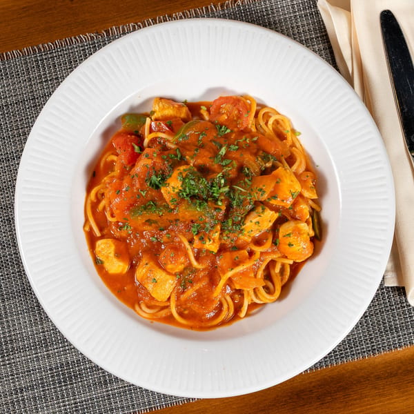 Spaghetti with chicken, bell peppers, and tomatoes in a rich red sauce, garnished with parsley.