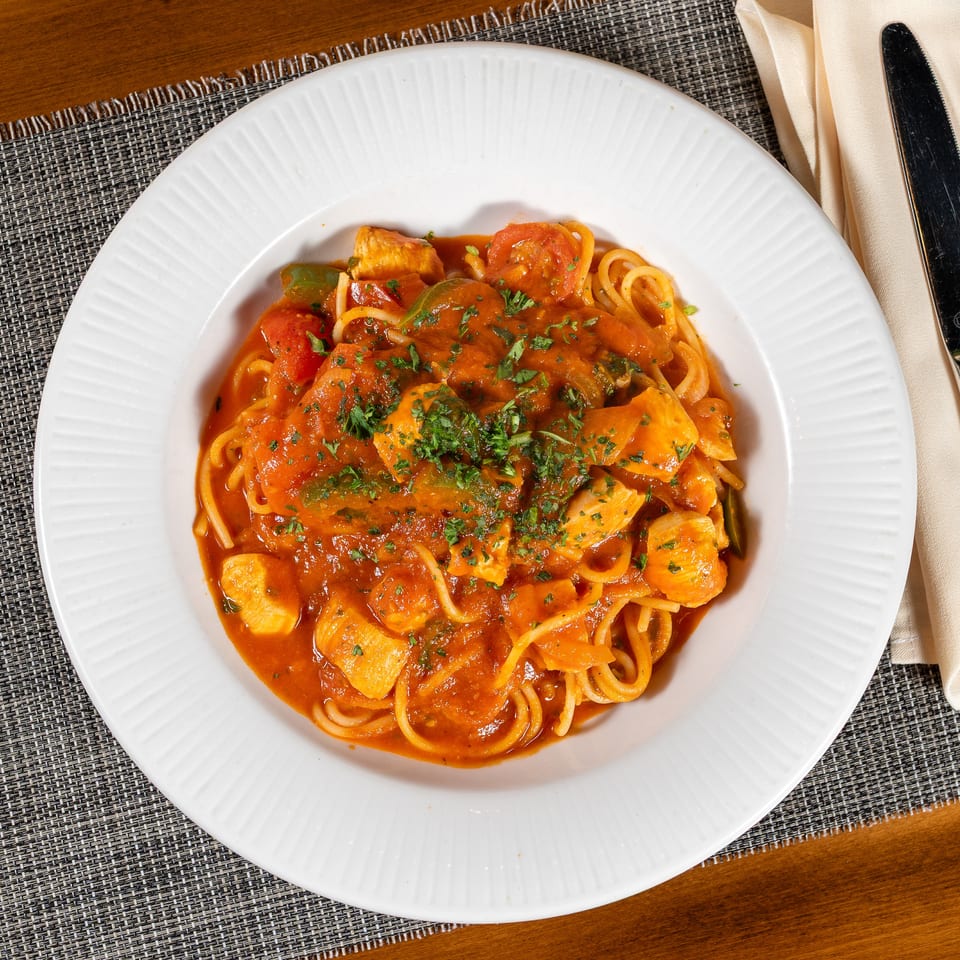 Spaghetti with chicken, bell peppers, and tomatoes in a rich red sauce, garnished with parsley.