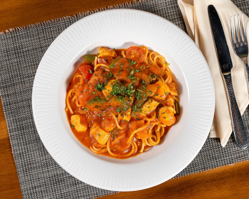 Spaghetti with chicken, bell peppers, and tomatoes in a rich red sauce, garnished with parsley.