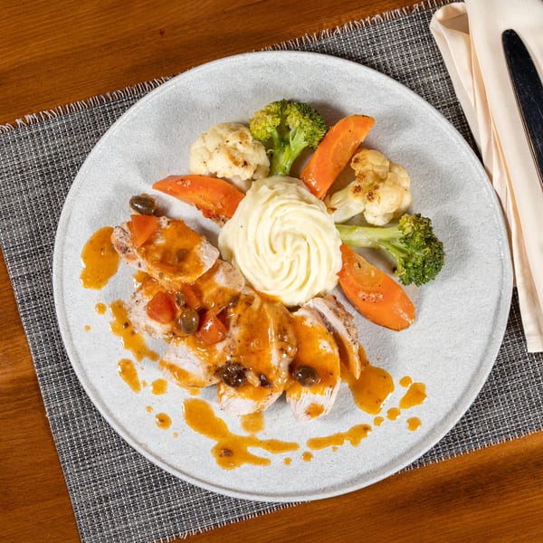 Sliced chicken with orange sauce, mashed potatoes, roasted carrots, broccoli, and cauliflower on a plate.