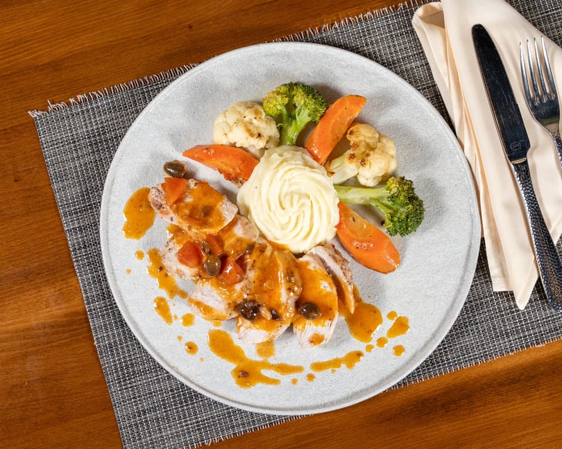Sliced chicken with orange sauce, mashed potatoes, roasted carrots, broccoli, and cauliflower on a plate.