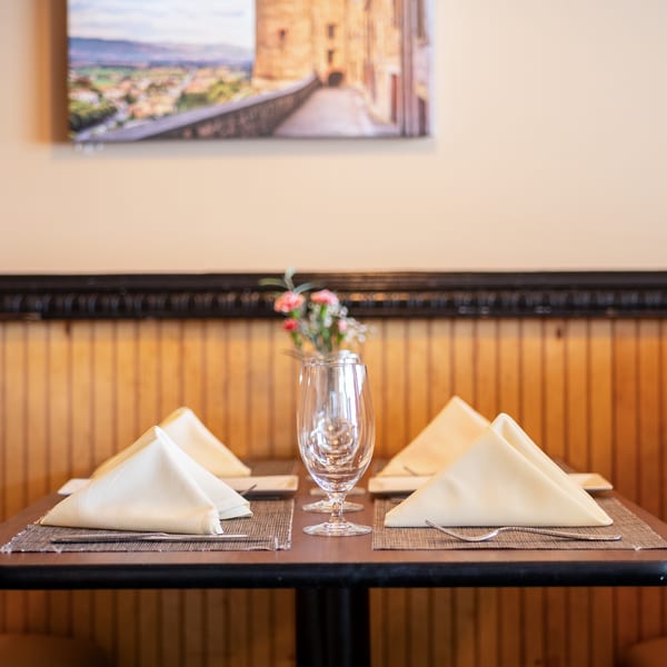 A restaurant table set with folded napkins, wine glasses, and a small vase of flowers.