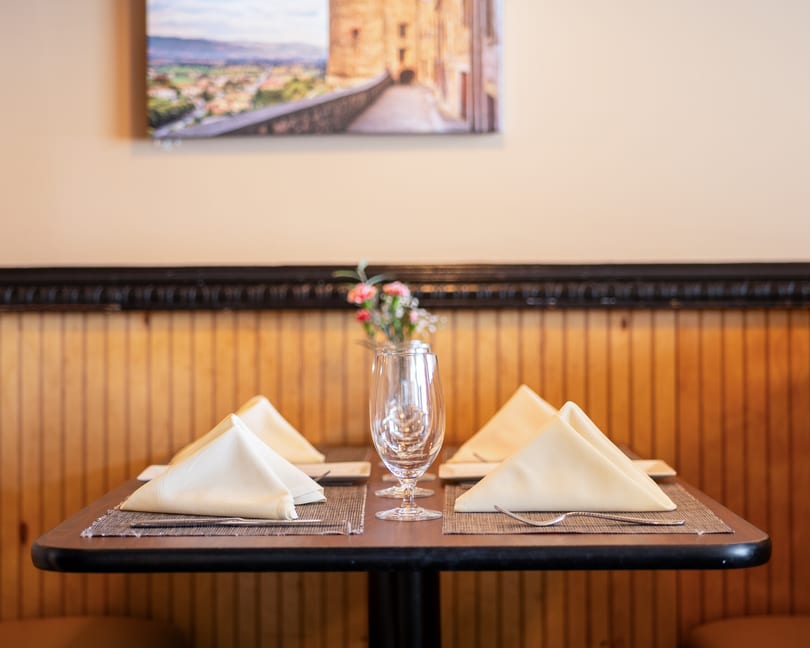 A restaurant table set with folded napkins, wine glasses, and a small vase of flowers.