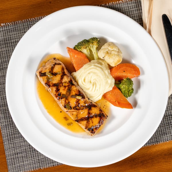 Grilled salmon with mashed potatoes, carrots, broccoli, and cauliflower on a white plate.