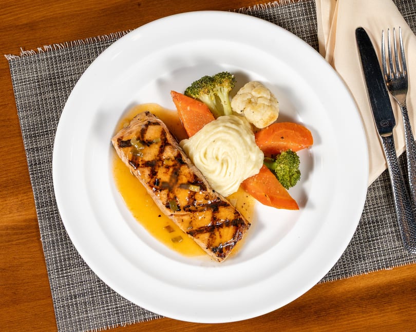 Grilled salmon with mashed potatoes, carrots, broccoli, and cauliflower on a white plate.